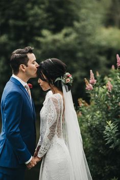 a bride and groom standing in front of some trees with their heads touching each other