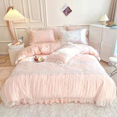 a bed with pink comforter and pillows in a room next to a lamp on a table