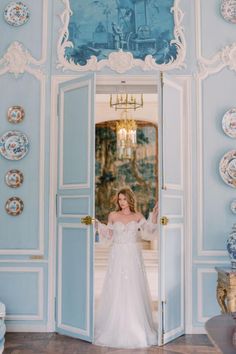 a woman in a wedding dress standing at an open door with plates on the wall behind her