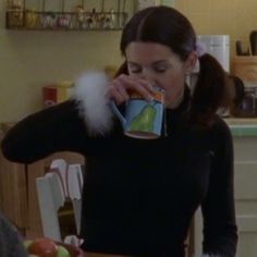 a woman drinking from a cup while standing in a kitchen