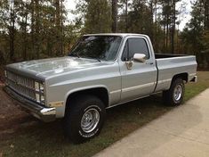 a silver pick up truck parked on the side of a road in front of some trees