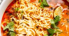 a white bowl filled with noodles and garnished with cilantro, parsley and lime