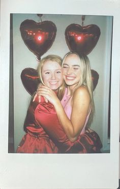 two girls hugging each other in front of heart shaped balloons