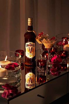 a bottle of alcohol sitting on top of a table next to glasses filled with candles