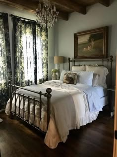 a bedroom with a bed, chandelier and two windows in the wall behind it