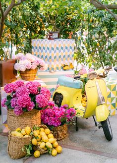 a yellow scooter with baskets full of flowers and lemons on the ground