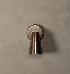 a wall mounted light on the side of a gray wall with a metal cone hanging from it's center