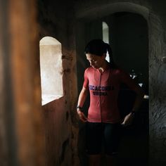 a woman in a red shirt standing next to a wall and looking at the camera