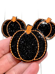 three black and orange pumpkins with glitter on them are being held by someone's hand