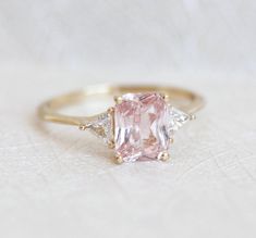 an engagement ring with a pink diamond and three diamonds on the side, sitting on a white surface