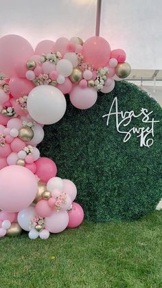 pink and white balloons are on display in front of a large green wall with an arch