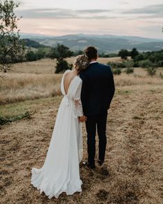 a bride and groom standing in the middle of a field looking out at the mountains