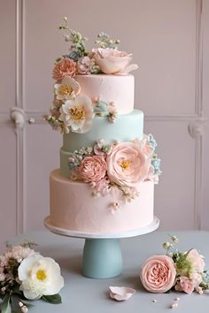 a three tiered cake with pink and blue flowers on the top is sitting on a table