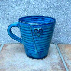 a blue cup with a heart on it sitting on a tile floor next to a wall