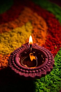 happy diwali greeting card with colorful background and lit candle on the ground in front of it