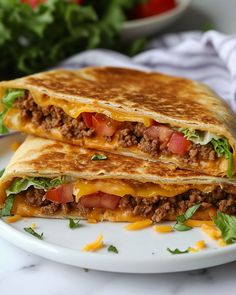 two quesadillas on a white plate with lettuce and tomatoes in the background