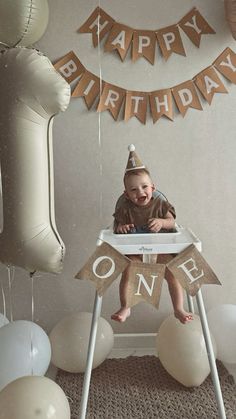 a baby is sitting in a highchair with balloons and streamers around him