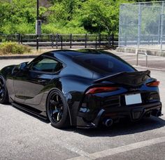 the rear end of a black sports car parked in a parking lot next to trees