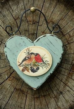 a wooden heart with a bird painted on the side and berries hanging from it's sides