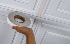 a hand holding a roll of toilet paper in front of a door with white paneling