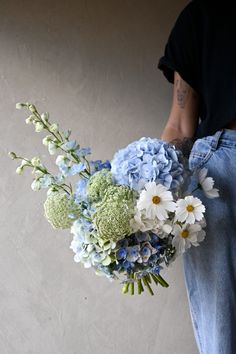 a person holding a bouquet of blue and white flowers in their left hand while standing next to a wall