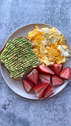 a plate with eggs, avocado and strawberries on it next to toast