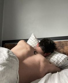 a shirtless man laying in bed with his head on the pillow and eyes closed