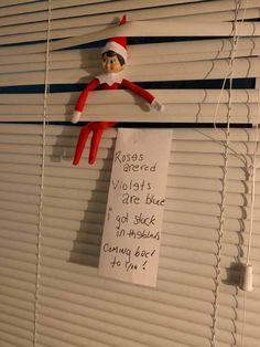 an elf is hanging on the blinds with a note attached to it