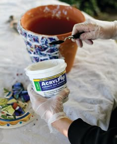 a person in white gloves is painting a pot with acrylic paint on it