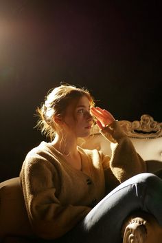 a woman sitting on top of a couch holding her hand up to her face and looking off into the distance