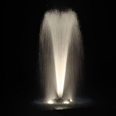 an illuminated fountain in the dark with water spewing from it's sides