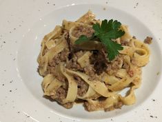 a white plate topped with pasta covered in meat and parsley on top of it