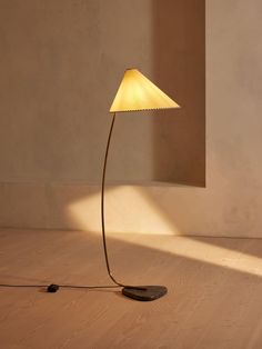 a floor lamp with a white shade on it in an empty room next to a wall