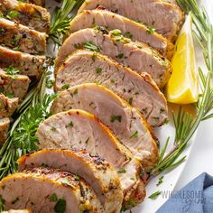 sliced pork with herbs and lemons on a white plate