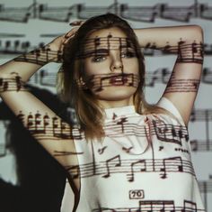 a woman with music notes painted on her body and hands behind her head, standing in front of sheet music