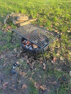 an outdoor grill is set up in the grass with rocks and leaves around it, next to a fire pit