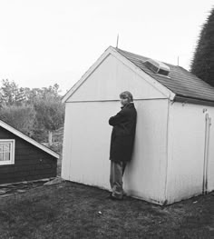 black and white photograph of a man leaning against a shed