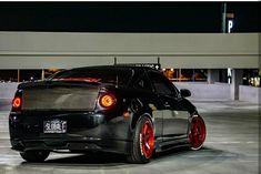 a black car with red rims parked in an empty parking lot at night time