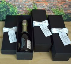 three black boxes with wine bottles wrapped in white ribbon and tags on them, sitting next to each other