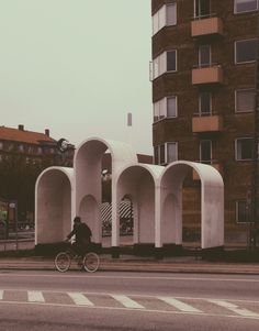 a person riding a bike down a street next to tall white arches on the side of a building