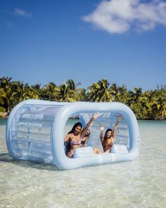 two women are in an inflatable pool on the beach with palm trees behind them