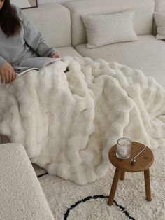 a woman sitting on top of a white couch under a blanket