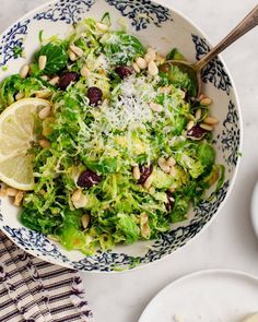 a salad in a bowl with lemon wedges and parmesan cheese