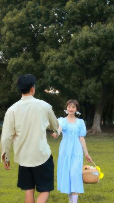 a man and woman walking across a lush green field holding baskets filled with flowers in their hands