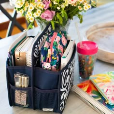 a desk with flowers, pens and notebooks on it next to a pen holder