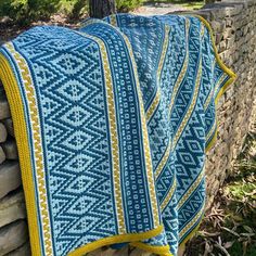 a blue and yellow blanket sitting on top of a stone wall next to a tree