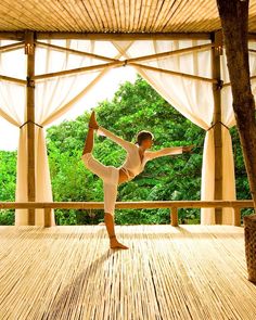 a person doing yoga on a wooden floor in front of some trees and white curtains