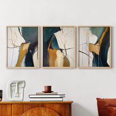 three paintings hanging on the wall above a dresser and sideboard in a living room