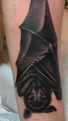 a black and white tattoo with a bat on it's leg that is upside down