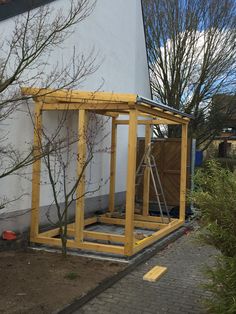 a small wooden structure sitting next to a tree in front of a white building with yellow trim